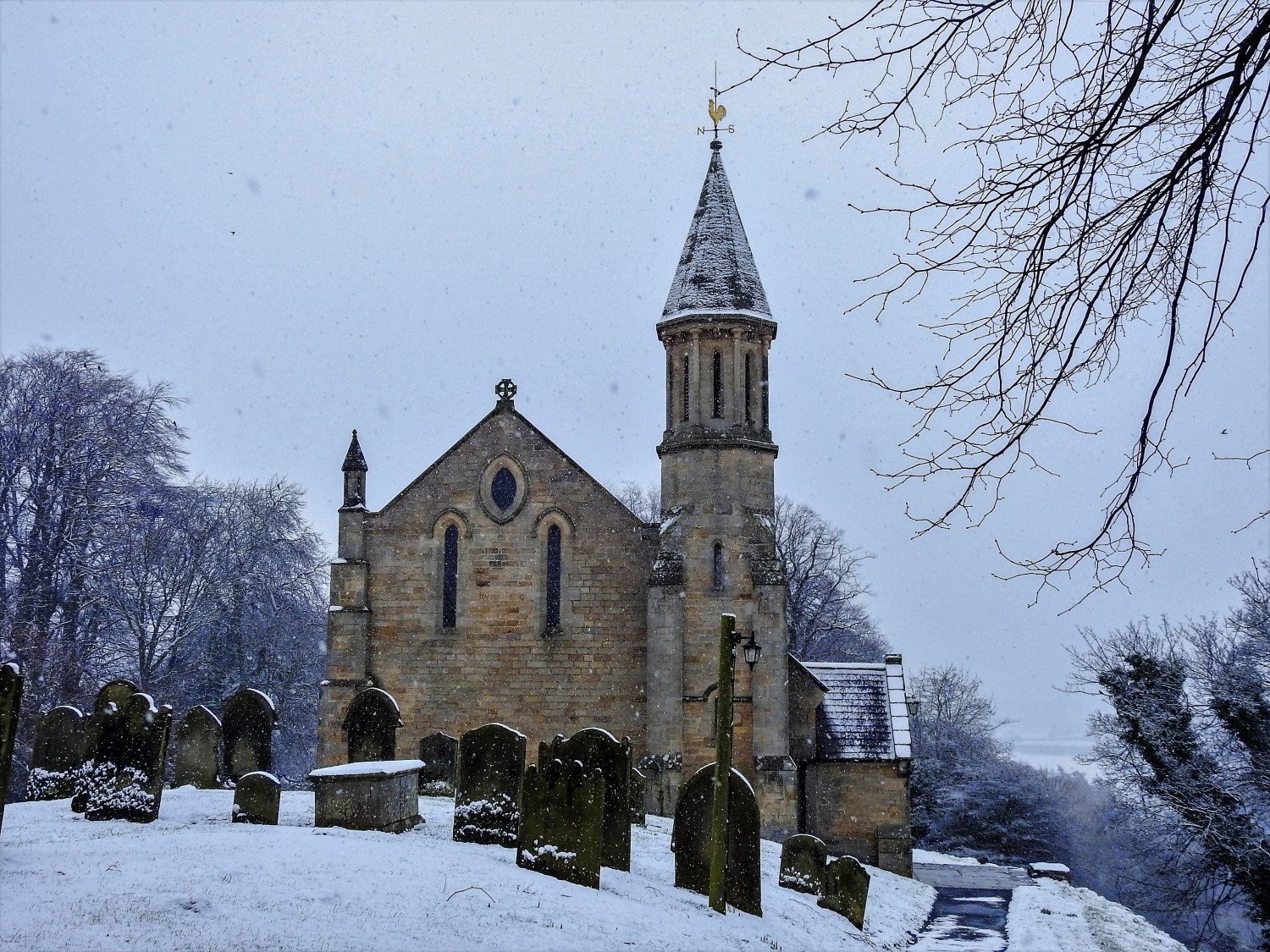 Church with gravestones in foreground. Grey sky and snow on the ground.